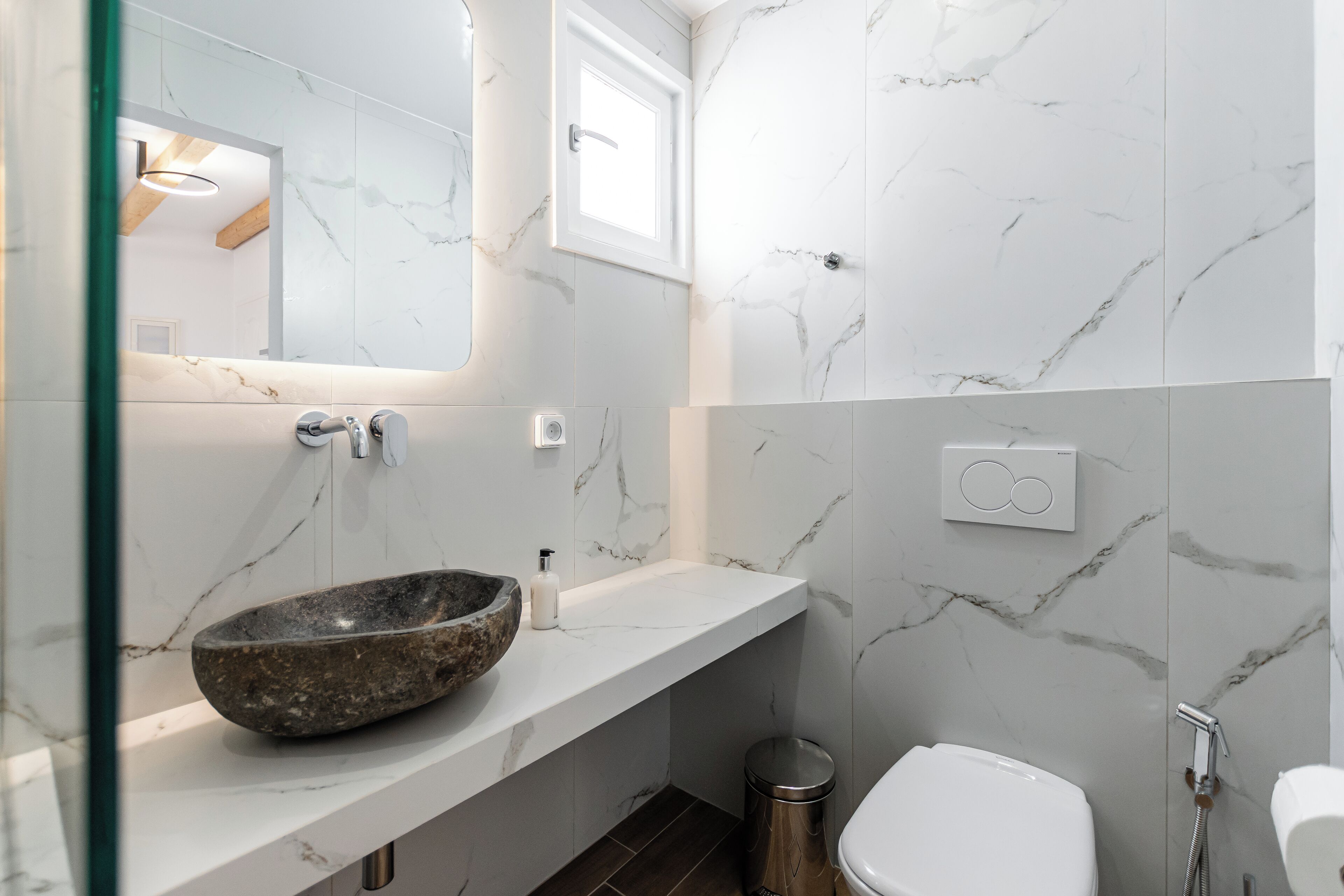 Un baño moderno con detalles de mármol en el salpicadero, un lavabo de piedra, inodoro y ducha.