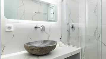 Un baño moderno con lavamanos de mármol, cabina de ducha de vidrio y un espejo grande sobre el lavamanos.