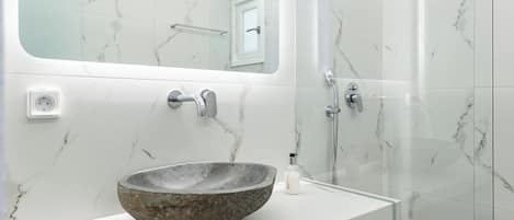A modern bathroom with a marble sink, a glass shower enclosure, and a large mirror above the sink.