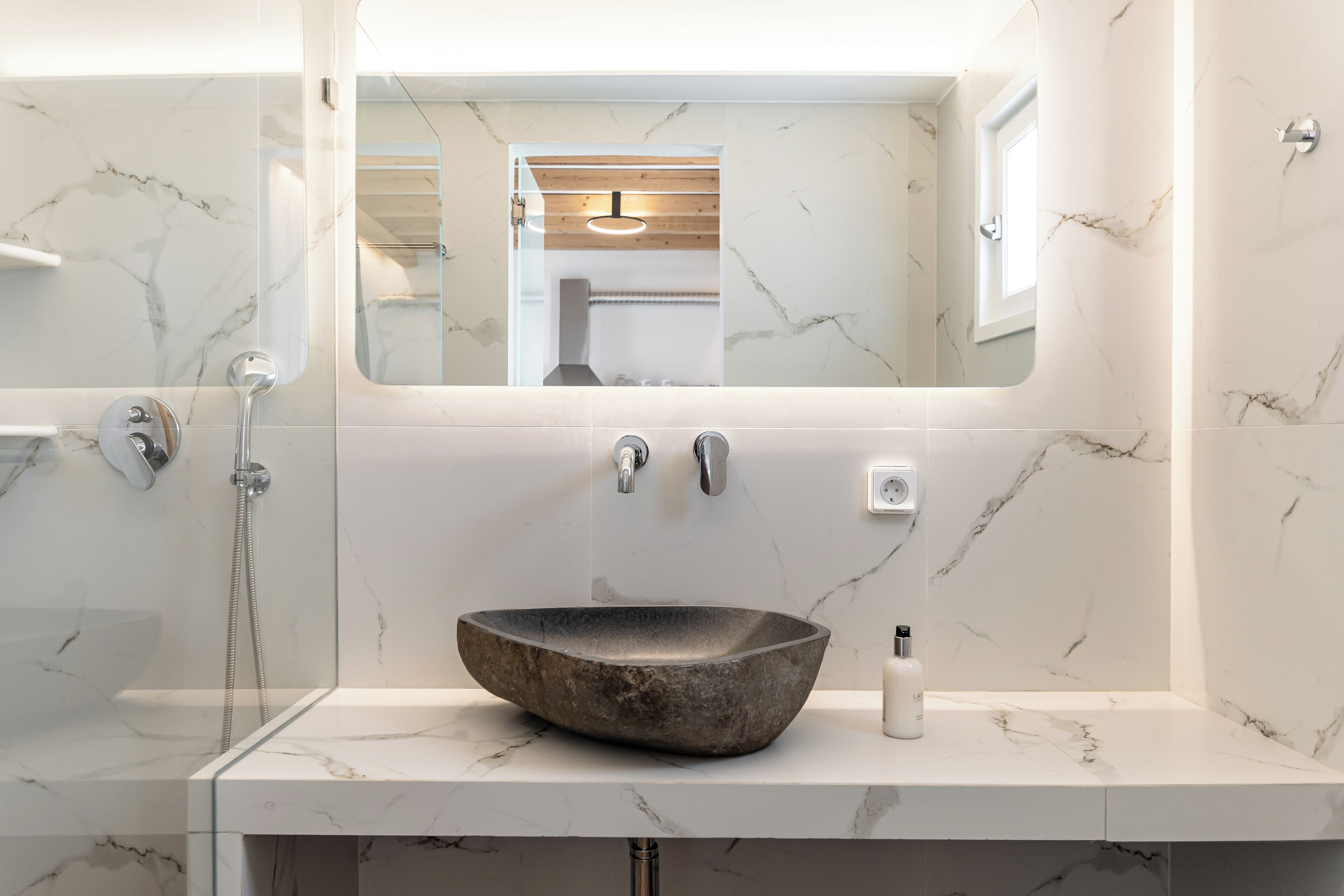 A bathroom with a large, dark stone sink, a glass-enclosed shower, and a mirror above the sink.