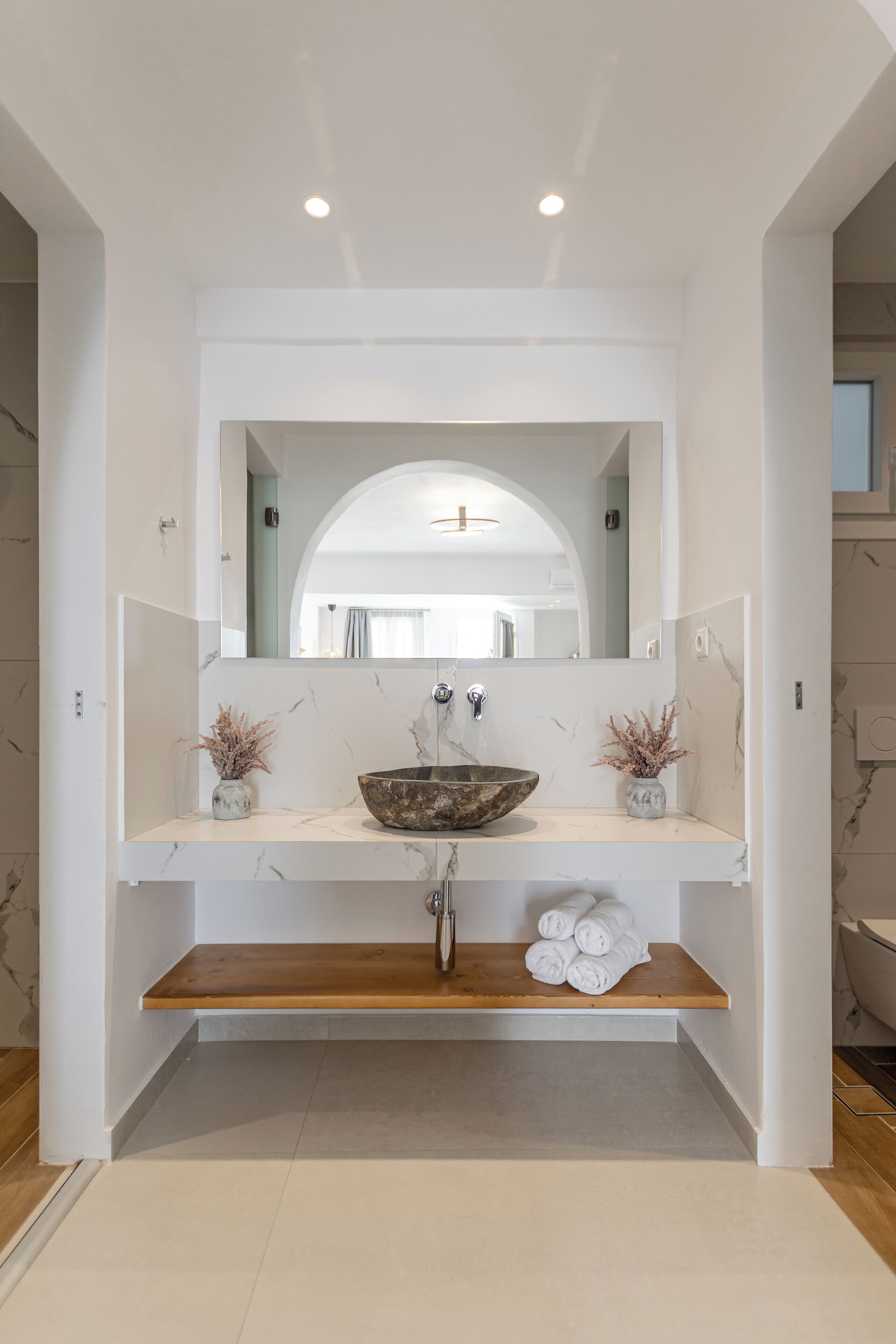 Un baño moderno con un espejo grande, un lavabo de mármol y dos pequeños jarrones sobre la encimera.