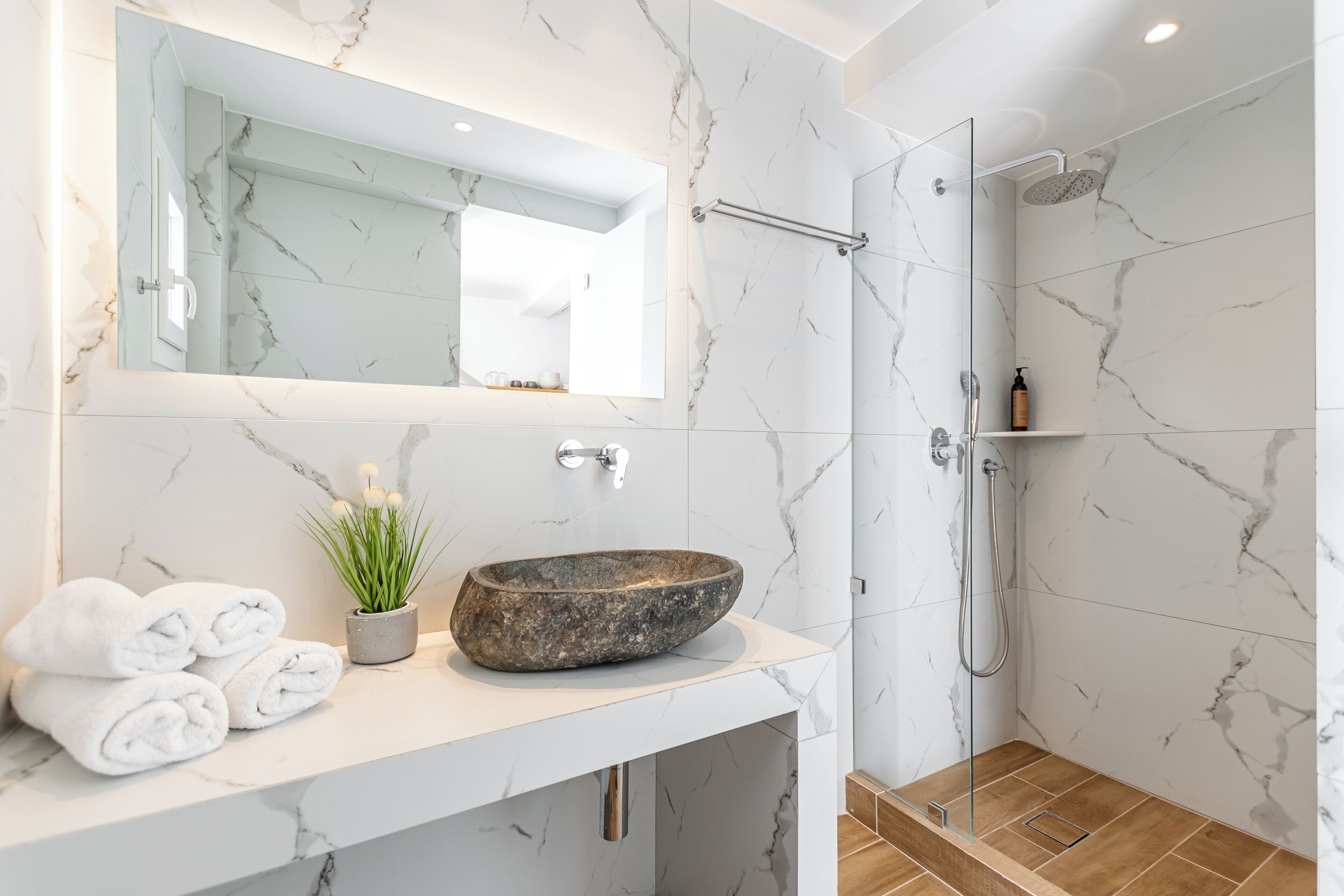 Un baño con tocador de mármol, un espejo grande, un lavabo de piedra y una zona de ducha.