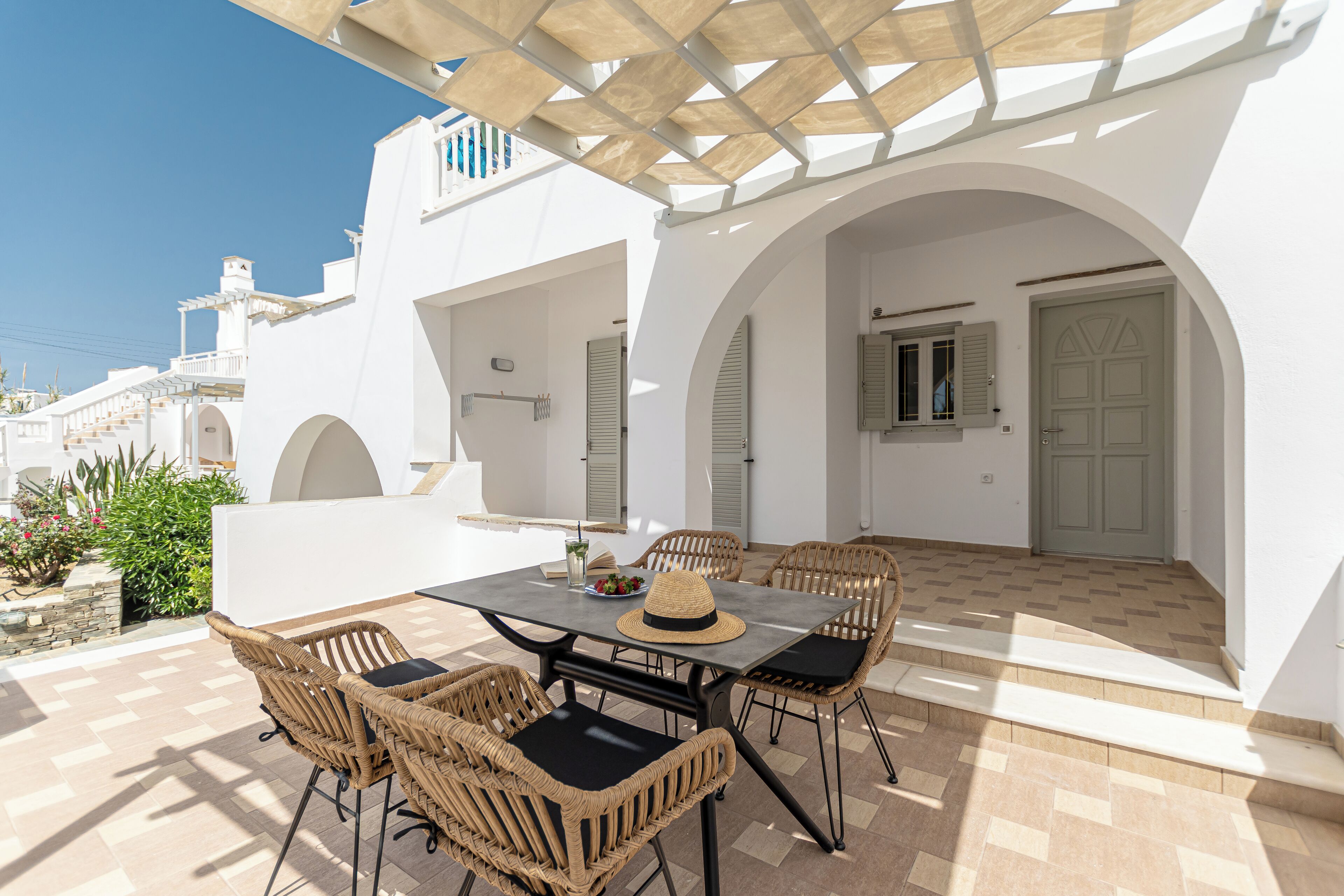 A white building with a covered patio, outdoor seating, and a view of the sea.