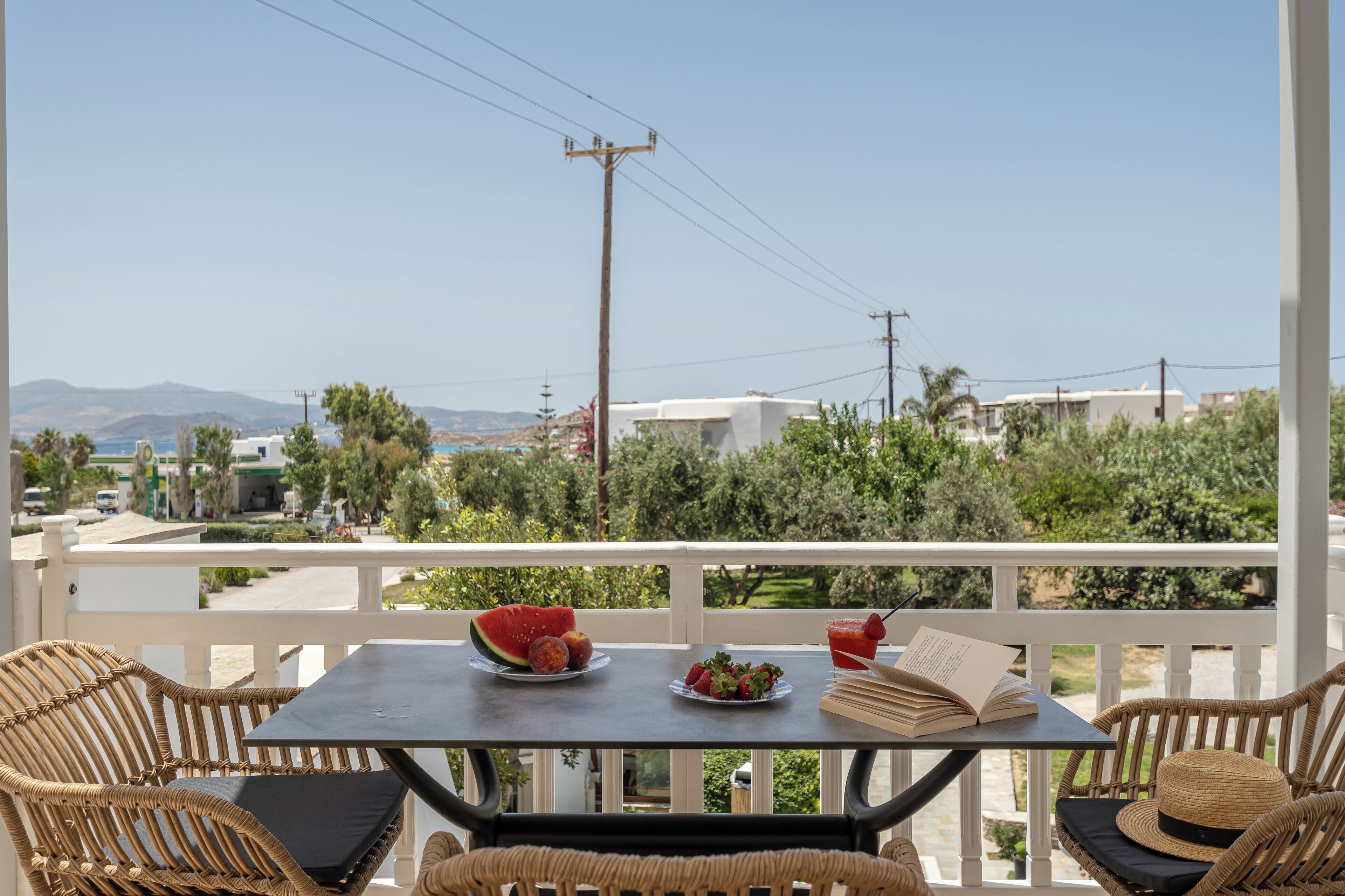 A balcony with wicker furniture, a table with a watermelon, strawberries, and a drink, and a book.