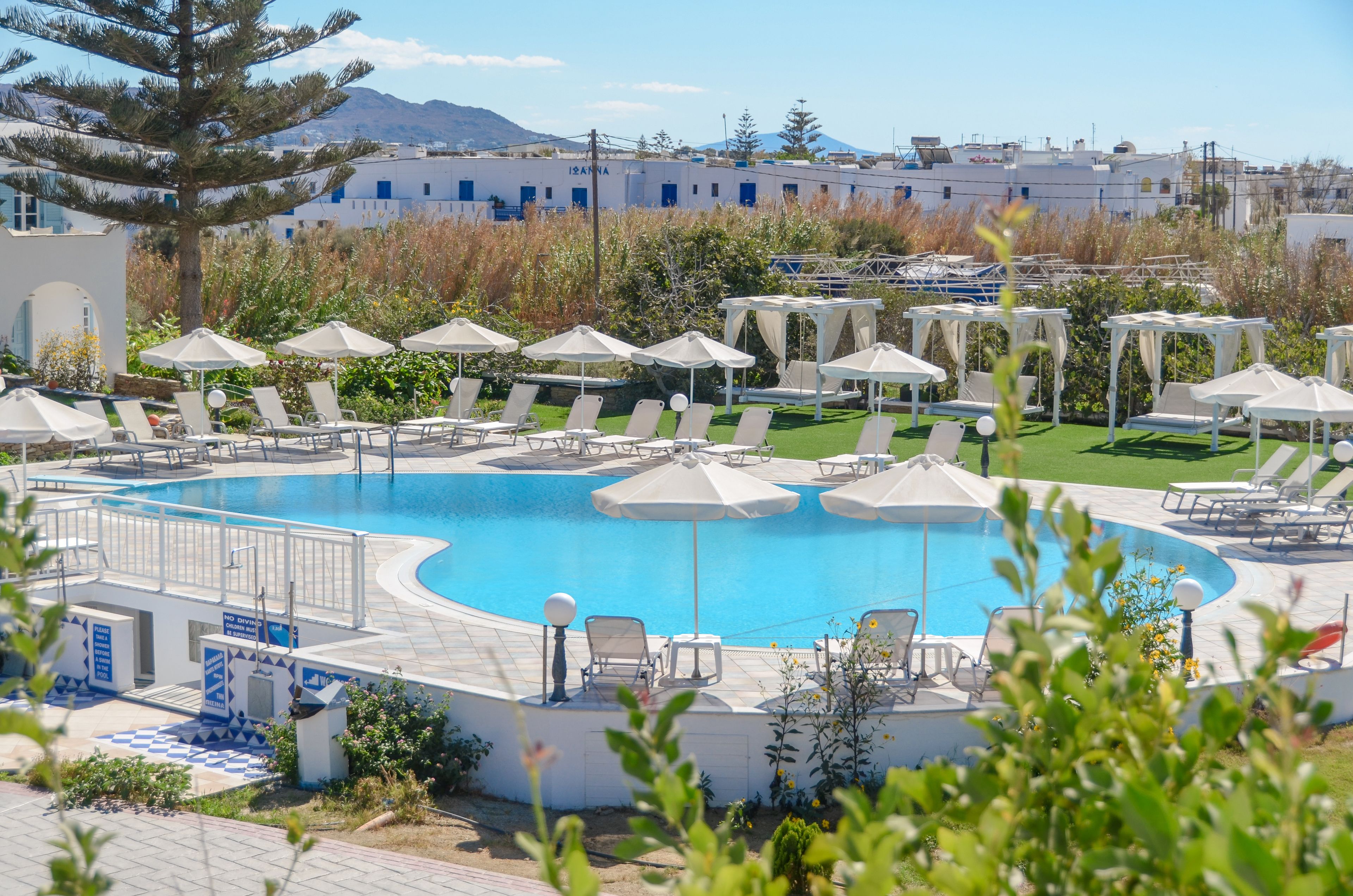A swimming pool with lounge chairs and umbrellas, surrounded by greenery and buildings in the background.