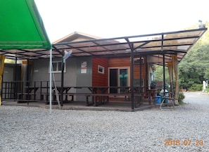A covered outdoor seating area with a wooden building in the background.