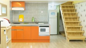 Ett kompakt kök med orange skåp, en mikrovågsugn och ett kylskåp. En trätrappa leder upp till en övre våning.