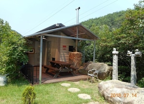 A small, rustic cabin with a metal roof, a brick chimney, and a picnic table.