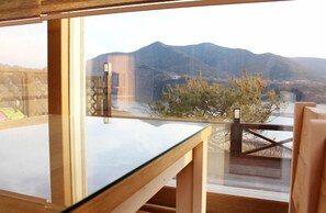 Una habitación con una mesa de vidrio y vistas a montañas y un puente.