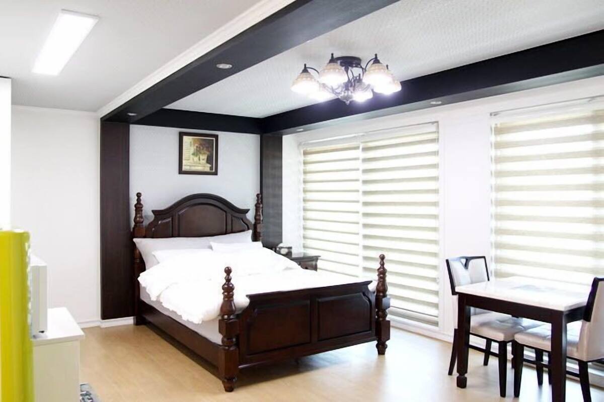 Une chambre à coucher avec un lit en bois, une table de chevet, une chaise et une fenêtre avec des stores.