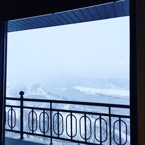 A view from a window with a metal railing, overlooking a snowy landscape with trees and a body of water. - Andong River Sunset Pension (Andong)