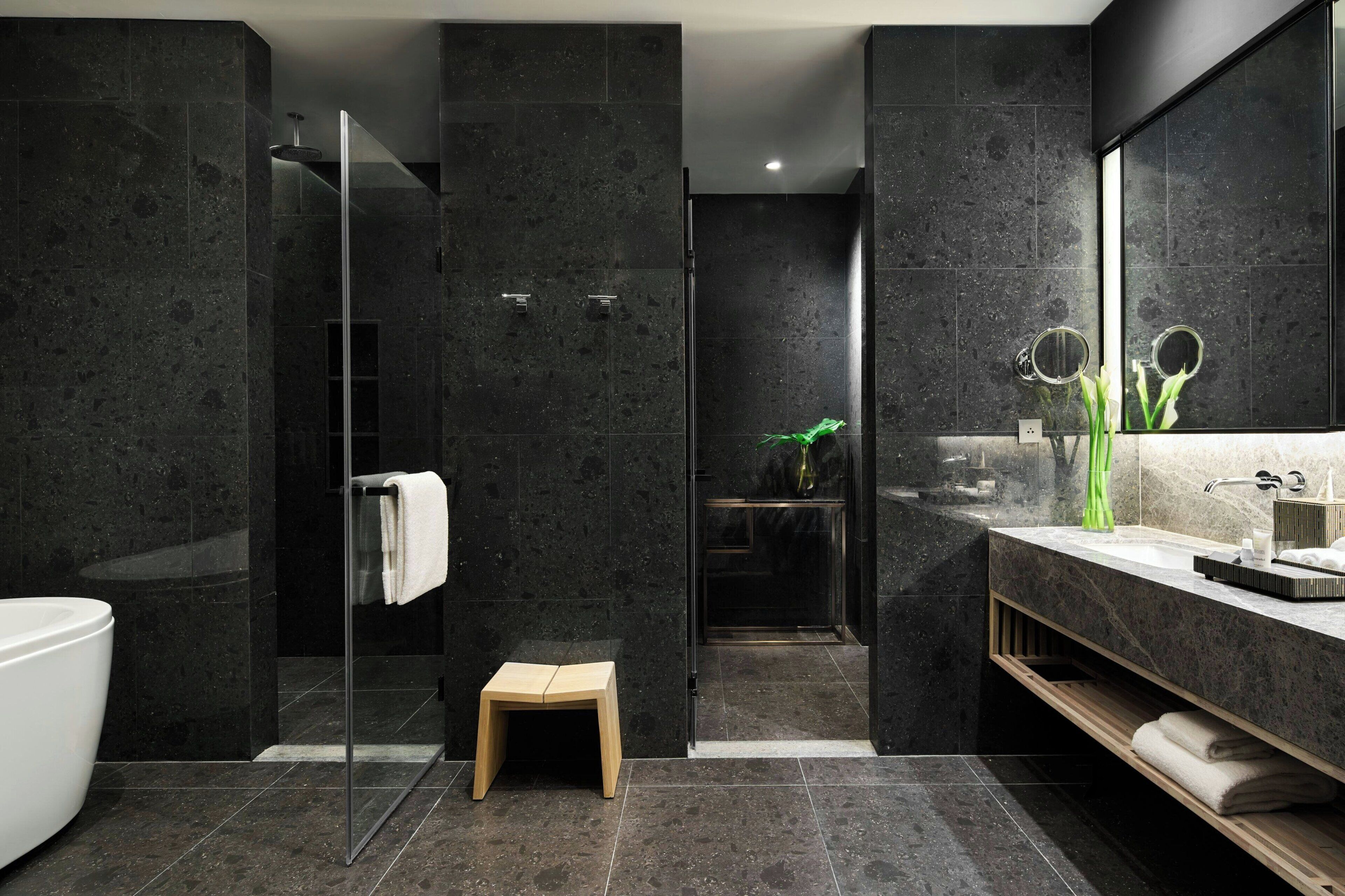 Une salle de bain moderne avec des murs en marbre foncé, une douche en verre, un tabouret en bois et un meuble-lavabo avec un miroir.