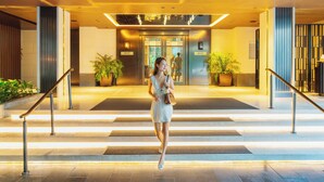 A woman walking towards an elevator in a modern building with a staircase, potted plants, and a well-lit entrance. - Marriott Executive Apartments, Bangkok Townhall Sukhumvit (Bangkok)