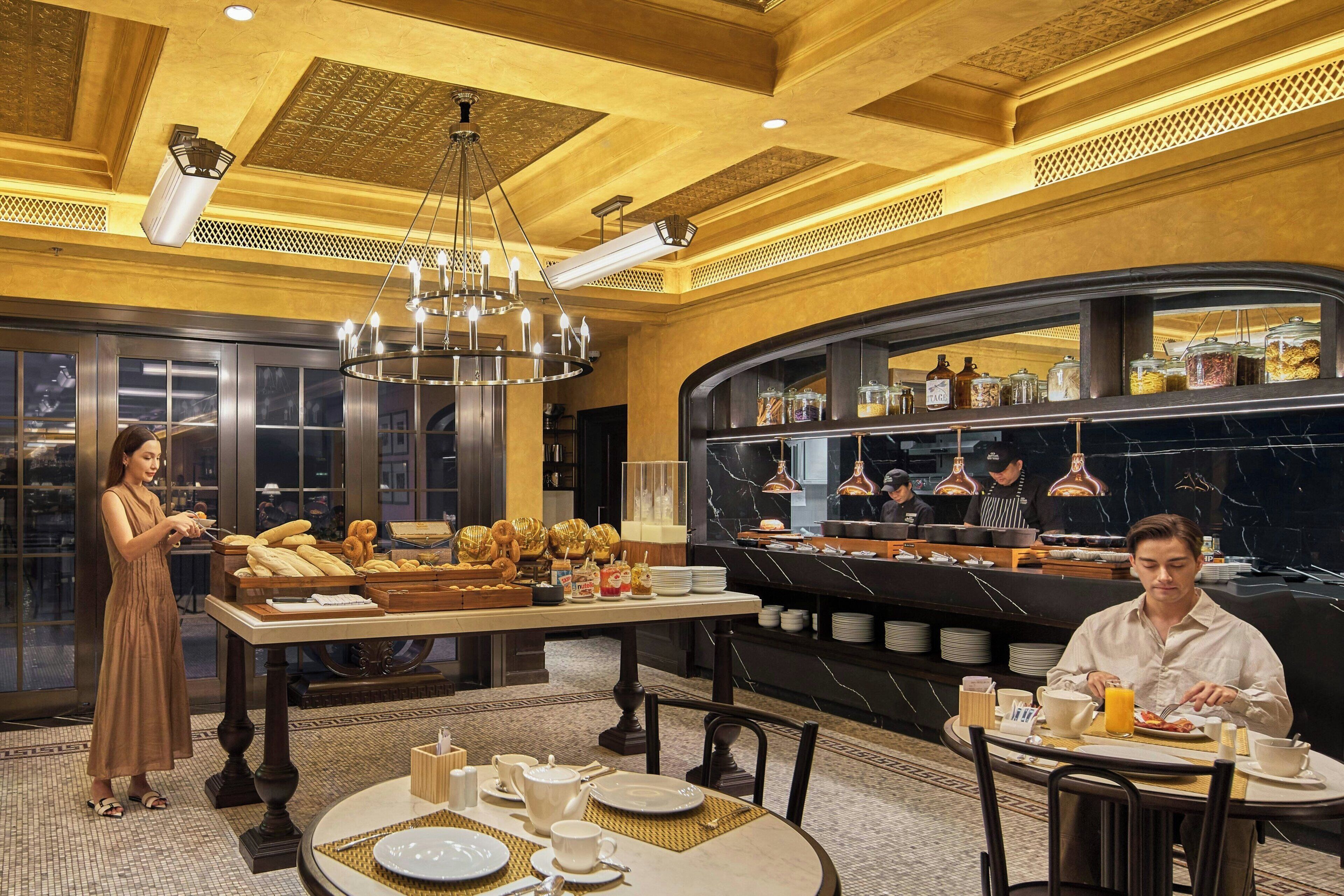 A breakfast buffet with a variety of food items and a woman serving food.
