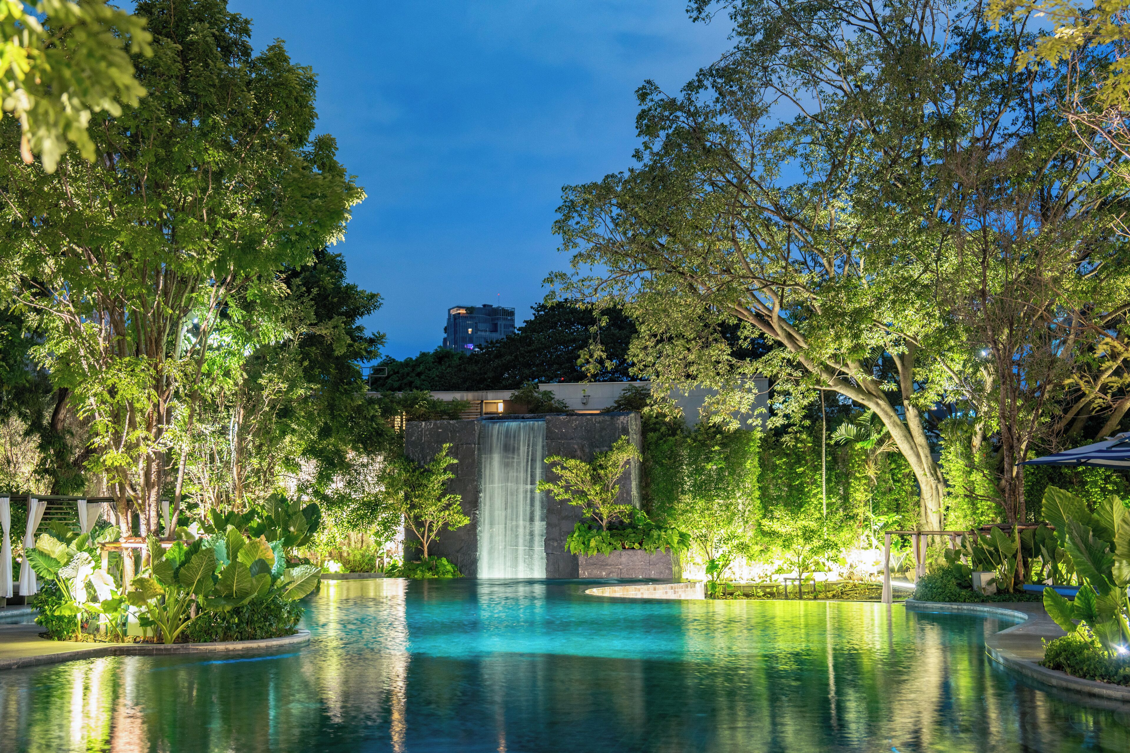A serene outdoor pool area with a waterfall, surrounded by lush greenery and trees.