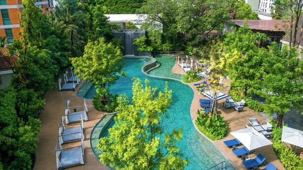An aerial view of a hotel pool area with a winding pool, lounge chairs, and umbrellas. - Marriott Executive Apartments, Bangkok Townhall Sukhumvit (Bangkok)