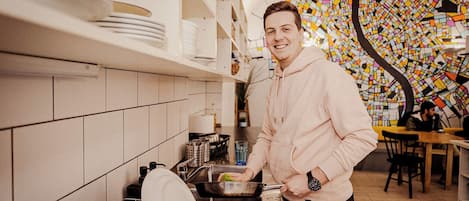 A person cooking in a kitchen with white cabinets, a tiled backsplash, and a colorful mosaic wall.