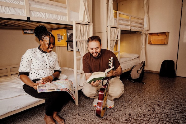 Una habitación con literas, una guitarra y una persona leyendo un libro.