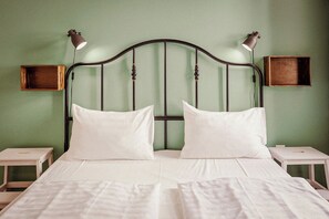 Un lit double avec deux oreillers, une tête de lit au design incurvé, deux tables de chevet et deux lampes fixées au mur.