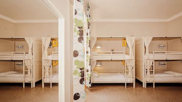 Una habitación con literas, piso de madera y cortina con diseño de hojas.