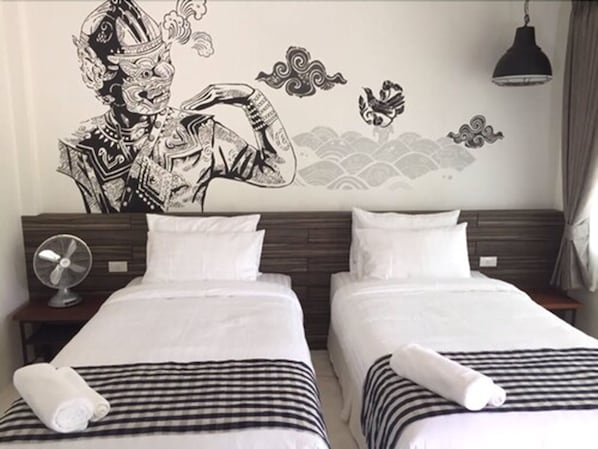A hotel room with two beds, a wall mural, a fan, and a hanging light fixture.