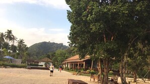 A beach with wooden benches, a covered seating area, and a view of a hill in the background.