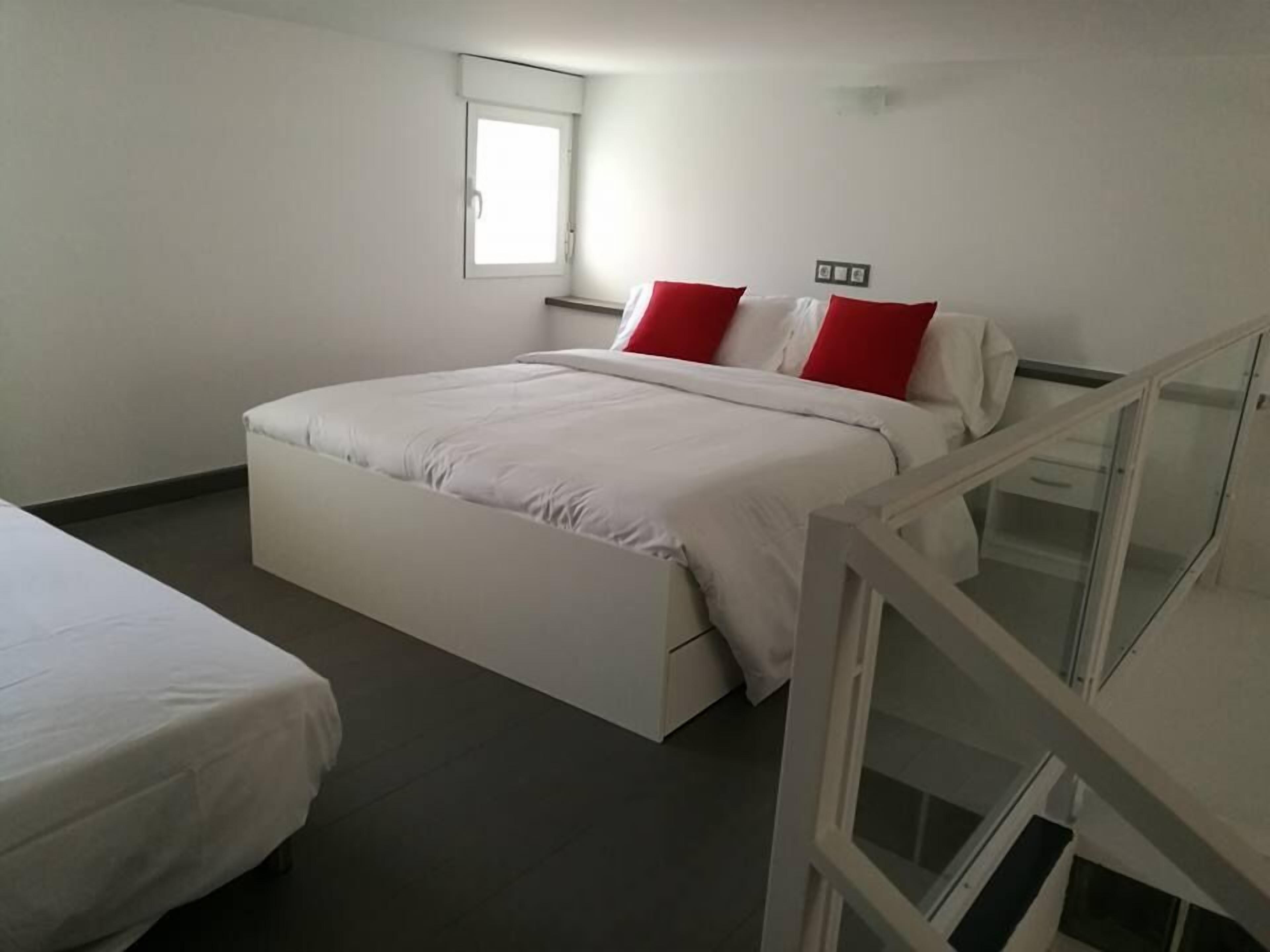 A bedroom with a bed, a window, and a bedside table.