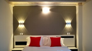 Habitación de hotel con una cama, dos almohadas rojas, ropa de cama blanca y dos luces fijadas a la pared.