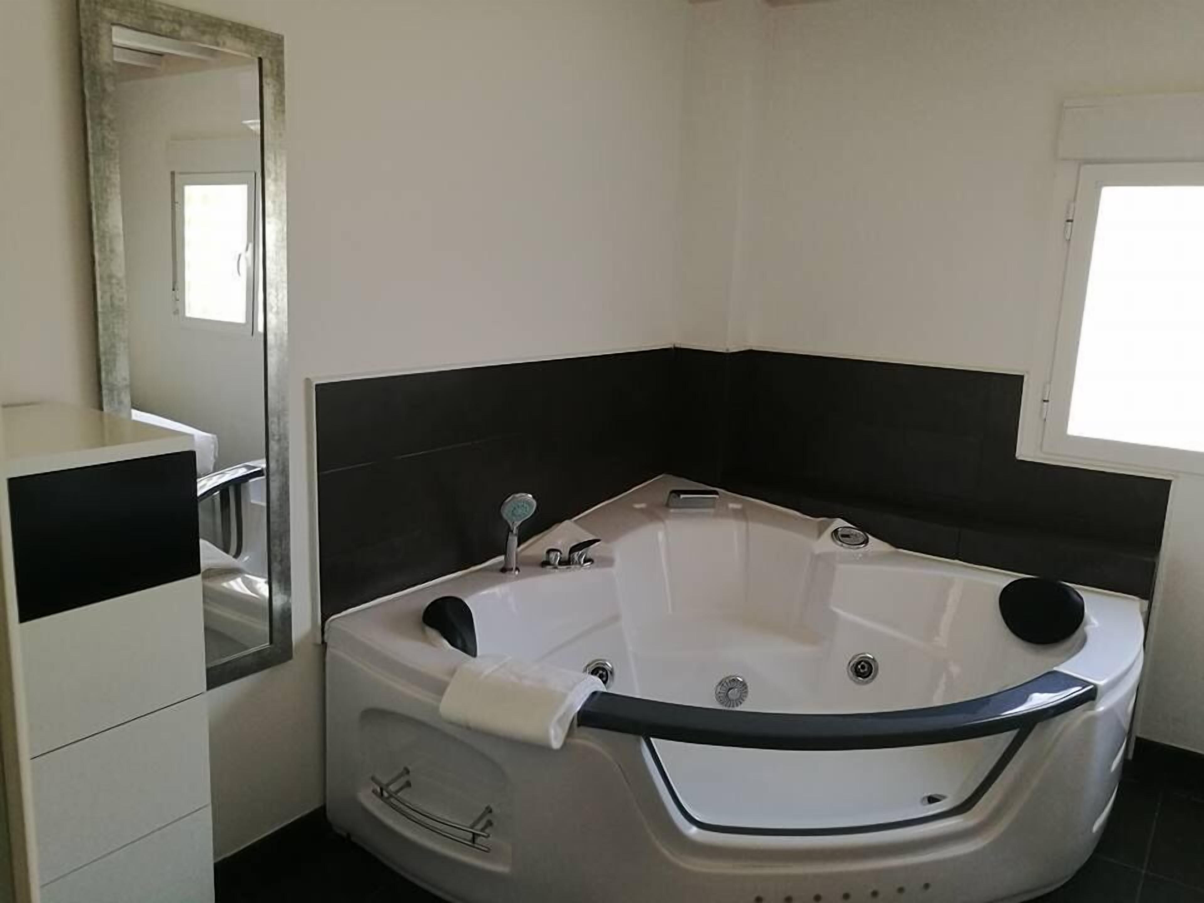 Casa de banho moderna com uma banheira de apoio, um espelho grande e um lavatório branco com bancada preta.