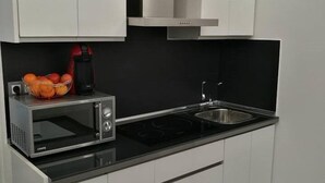 Una cocina compacta con microondas, pileta y una cesta de frutas.