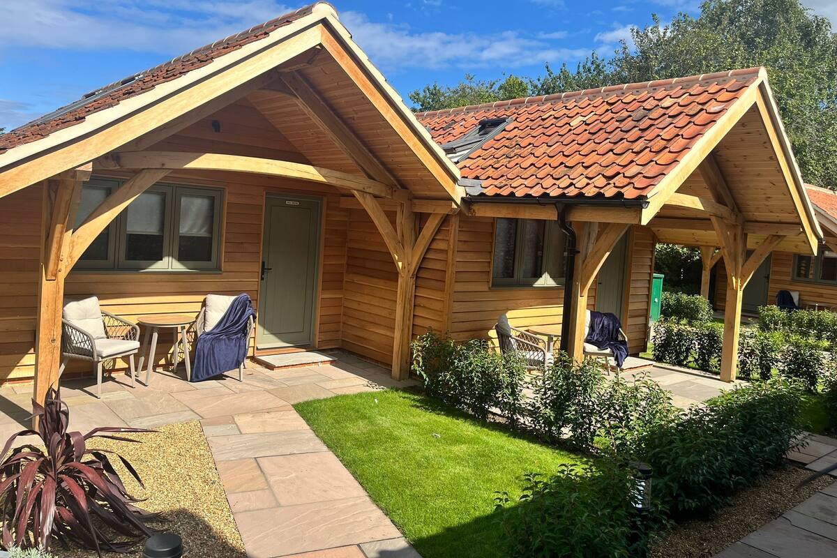 A wooden cabin with a tiled roof, a covered patio with outdoor seating, and a well-maintained lawn.