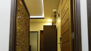 Um corredor com uma porta de madeira, um cesto de lixo e uma luminária.