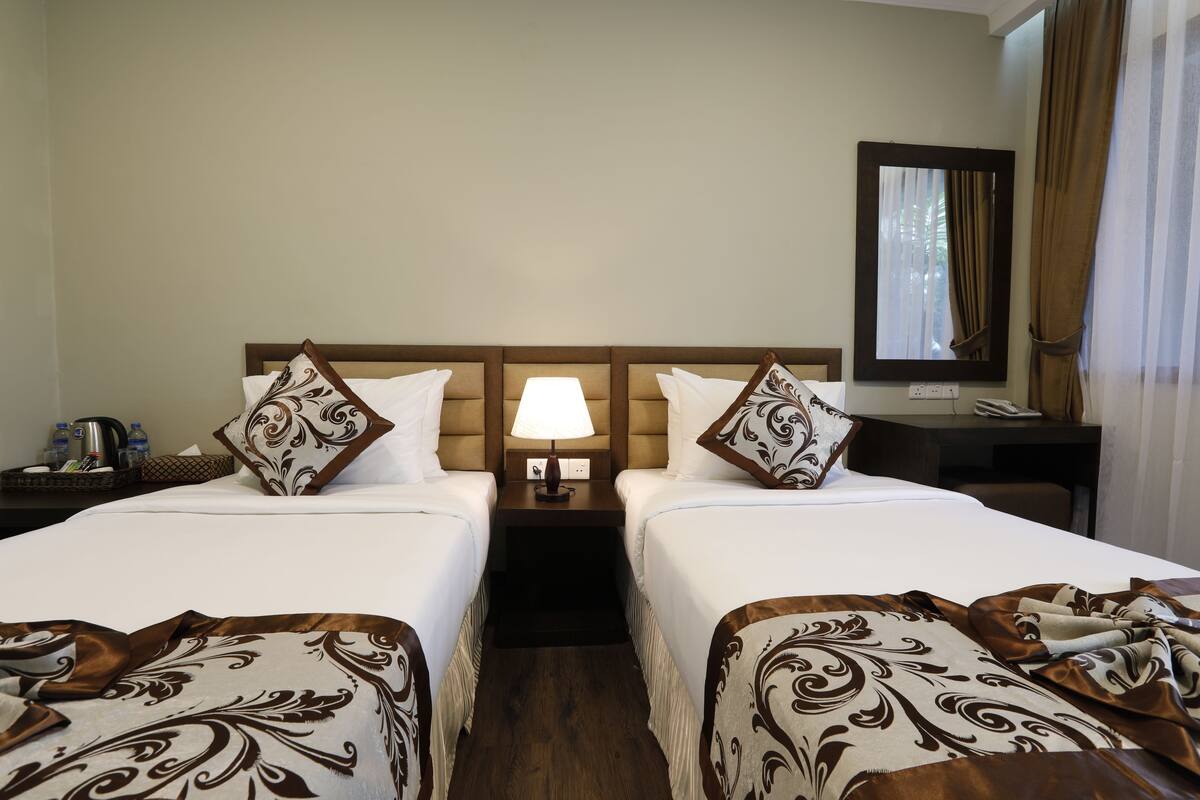 Une chambre d’hôtel avec deux lits, une table de chevet avec une lampe, un miroir et une petite table avec un téléphone et un panier.