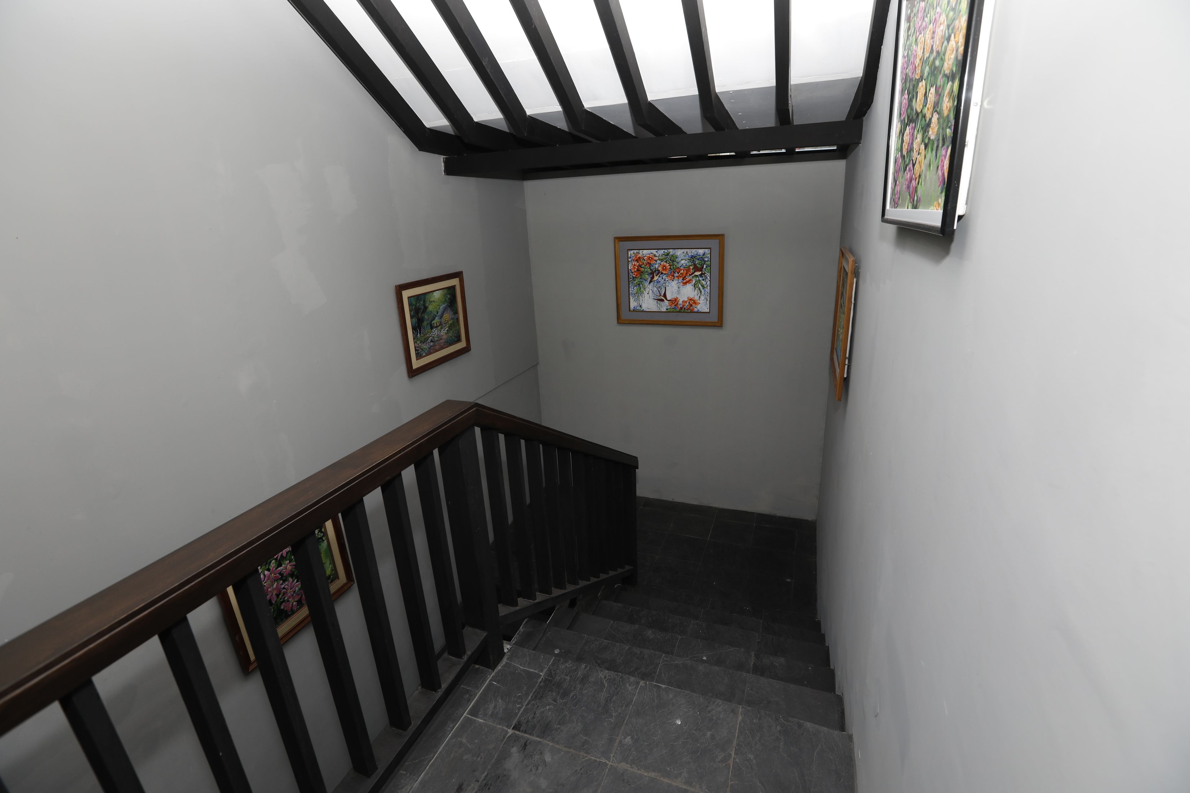 Una escalera con barandilla de madera y balaustrada negra, que conduce a un rellano con dos obras de arte enmarcadas en las paredes.