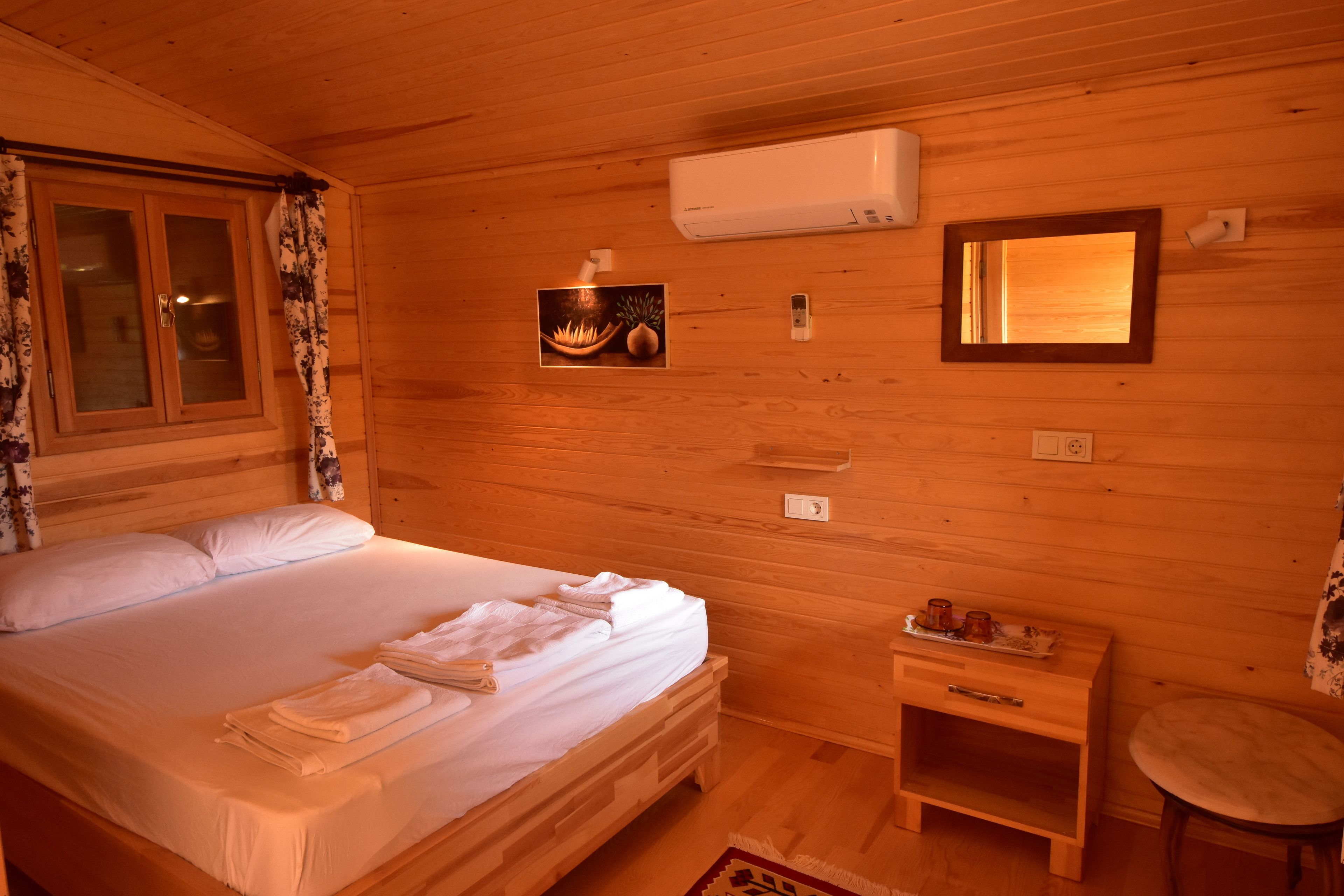 A wooden cabin room with a bed, a small wooden nightstand, a mirror, and an air conditioning unit.