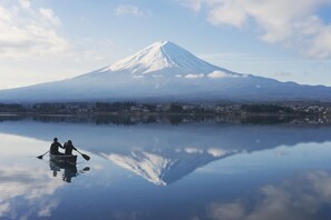 A calm lake with a reflection of a mountain and two people in a boat.