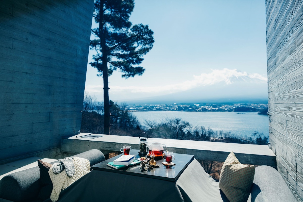 A balcony with a table set for tea, overlooking a scenic view of a lake and distant mountains.