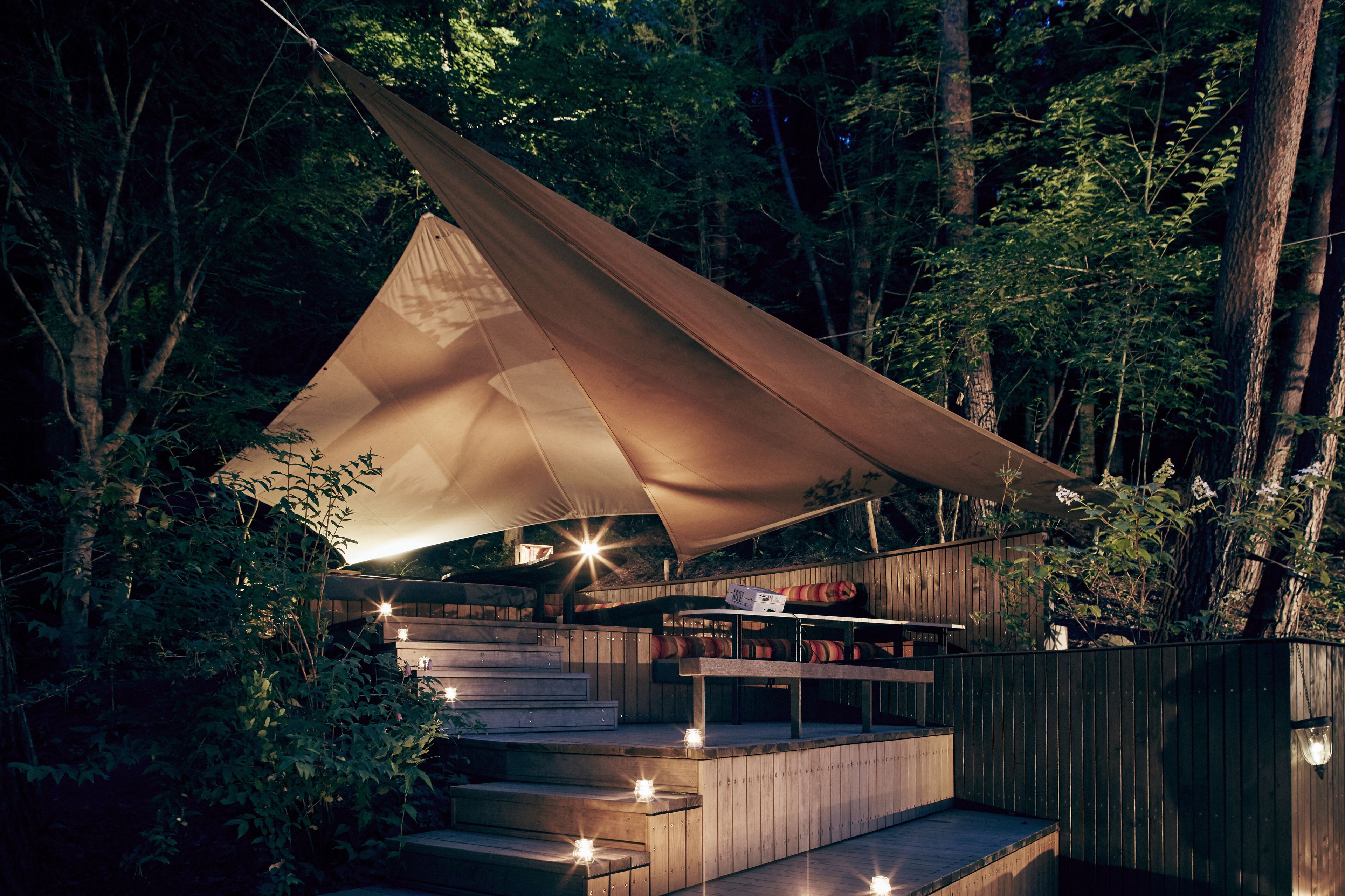 A tented outdoor area with a wooden deck and steps leading up to a platform with seating.