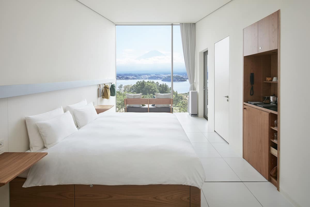 A modern hotel room with a large bed, wooden wardrobe, and a balcony with a view of a mountain and water.