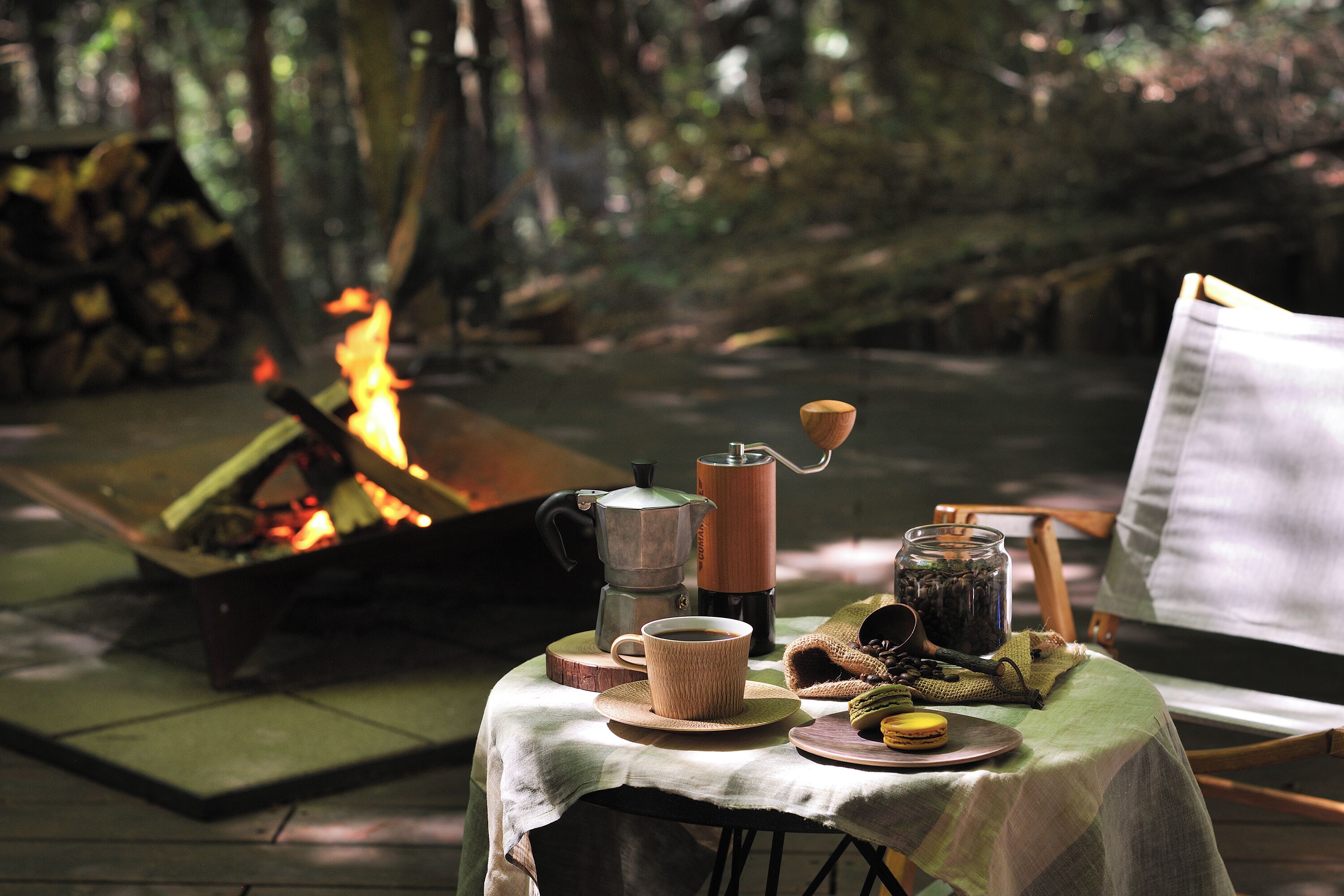 Mesa al aire libre con una chimenea, una cafetera, una taza y diferentes alimentos.