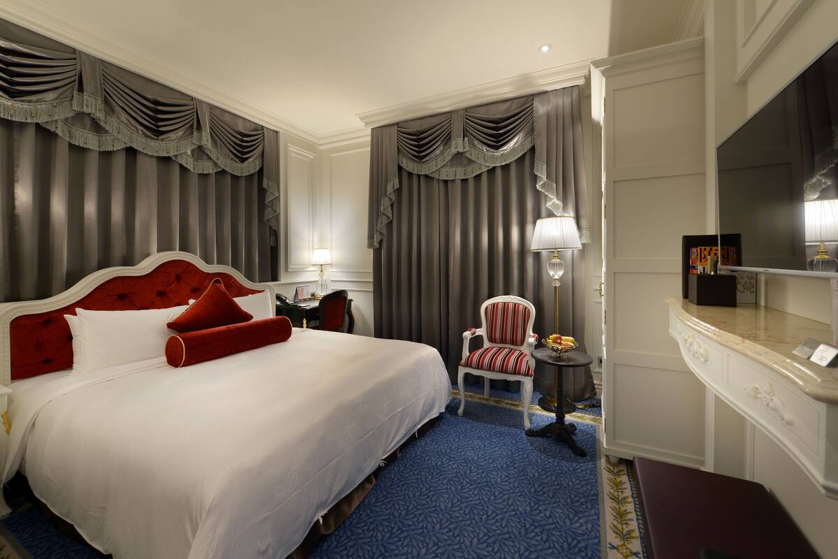 A hotel room with a large bed, a desk, a chair, a TV, and a minibar.