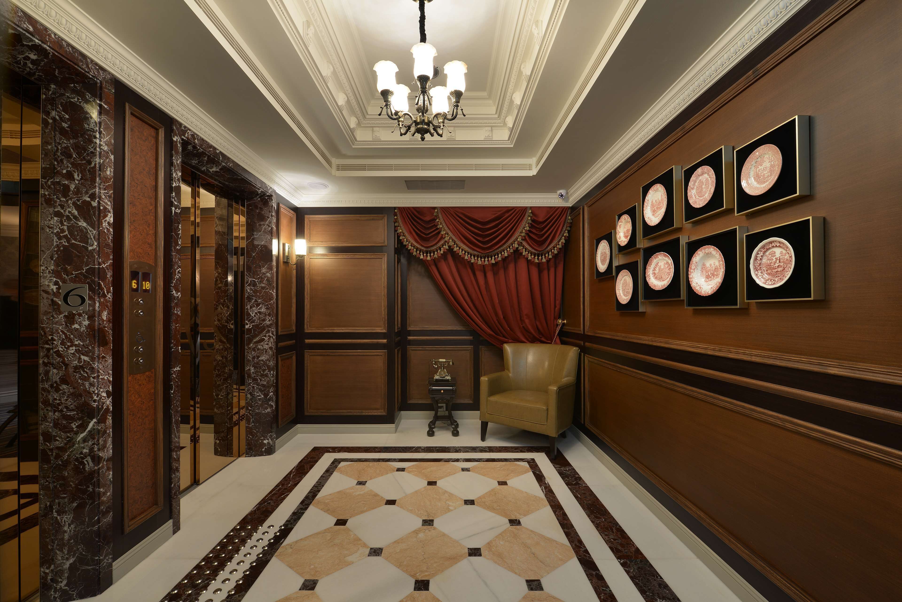 A luxurious lobby with marble walls, a patterned floor, a chandelier, a red curtain, and framed artwork.