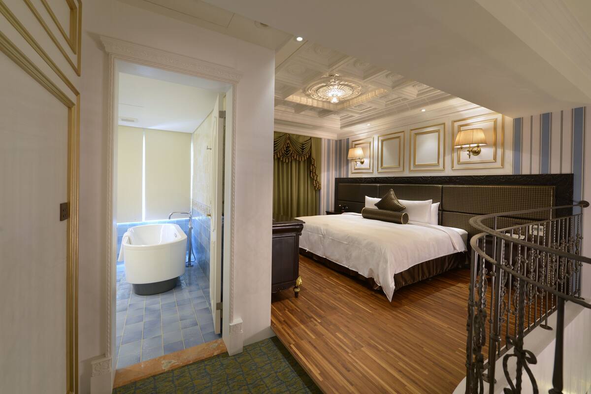 A bedroom with a large bed, a bathtub, and a staircase.