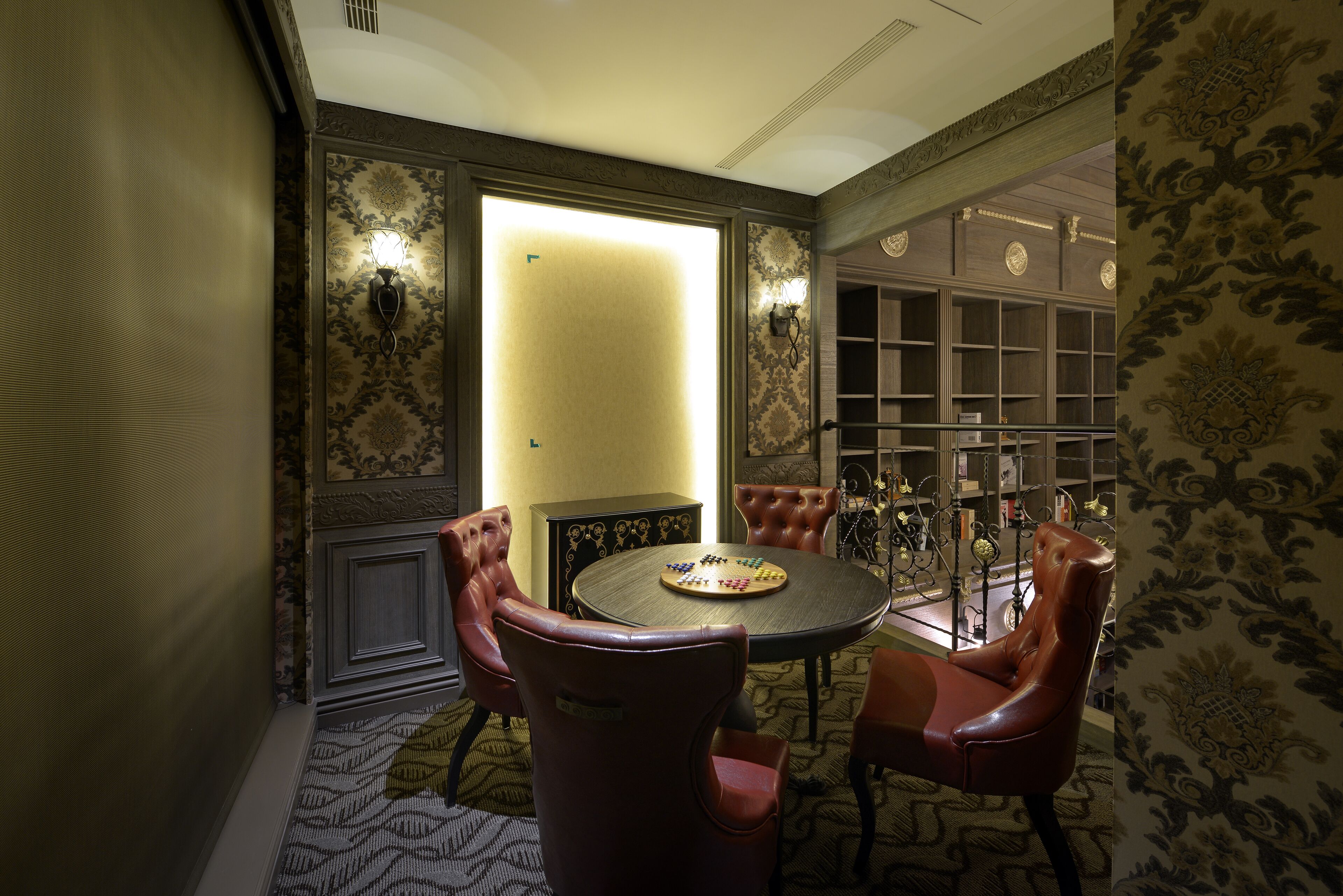 A room with a round table, leather chairs, a bookshelf, and patterned wallpaper.