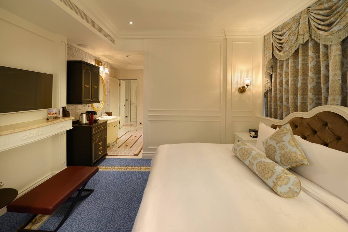 A hotel room with a large bed, a bench, a dresser, a mirror, and a television.