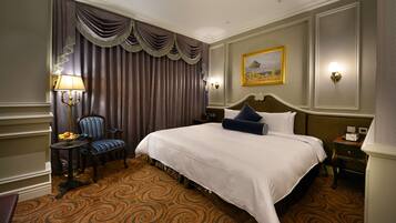 Habitación de hotel con una cama grande, una silla, una mesa con lámpara y un cuadro en la pared.