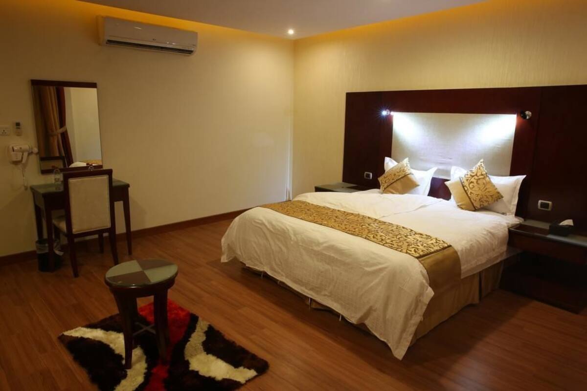 Ein Hotelzimmer mit einem großen Bett, Nachttischen, einem Schreibtisch und einer Klimaanlage.