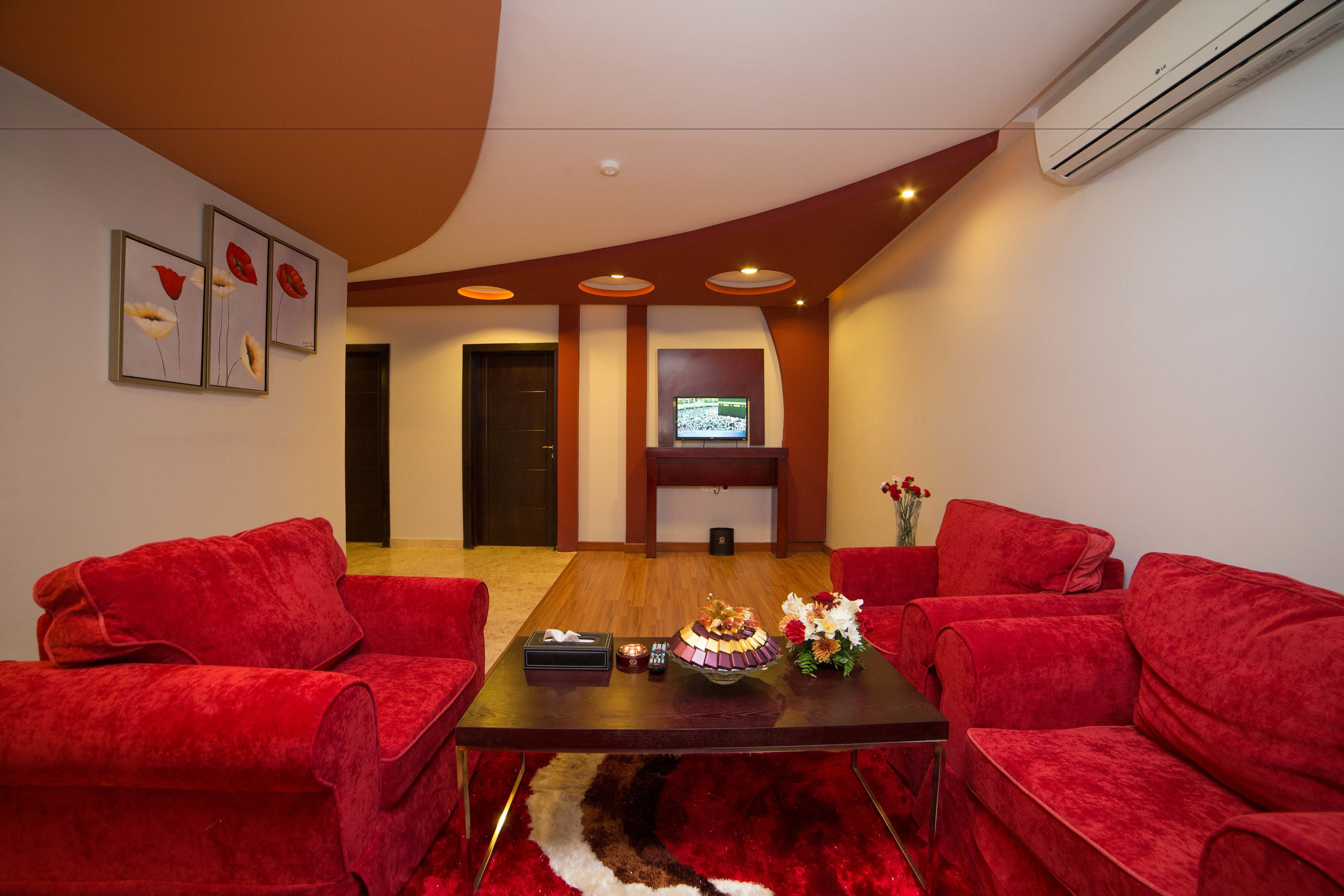 A modern living room with a red sofa set, a wooden coffee table, and a flat-screen TV mounted on the wall.