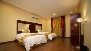 A hotel room with two beds, wooden flooring, a large mirror above the beds, a standing lamp, and a wall-mounted air conditioner. - Raoum Inn Hotel Apartments- Buraydah (Buraydah)