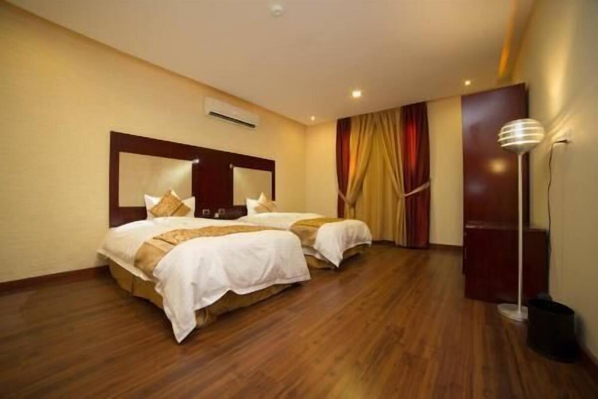 Ein Hotelzimmer mit zwei Betten, Holzboden, einer Deckenleuchte und einer Wandklimaanlage.